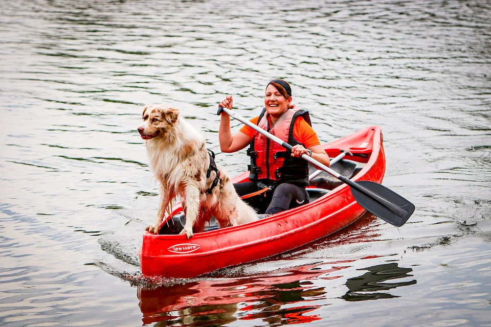 Marylon van Voerkrachtig in een rode kano met haar hond Fitz op een rustig meer tijdens een avontuurlijke hondvriendelijke activiteit